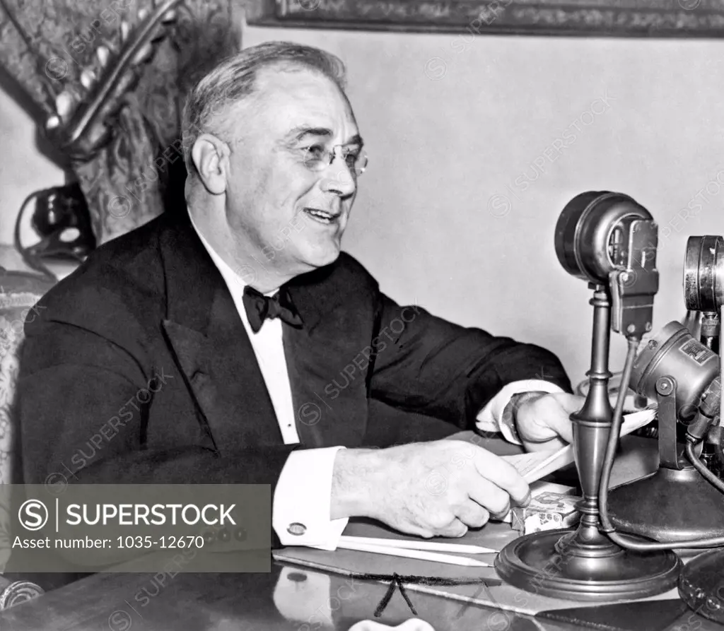 Washington, D.C.:  1937. President Franklin D. Roosevelt, seated behind microphone, during one of his fireside chats.