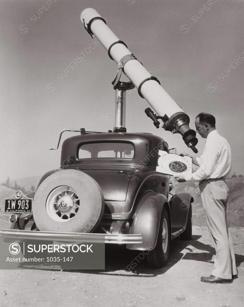 Stock Photo: 1035-147 Side profile of a mature man operating astronomy telescope, 1933