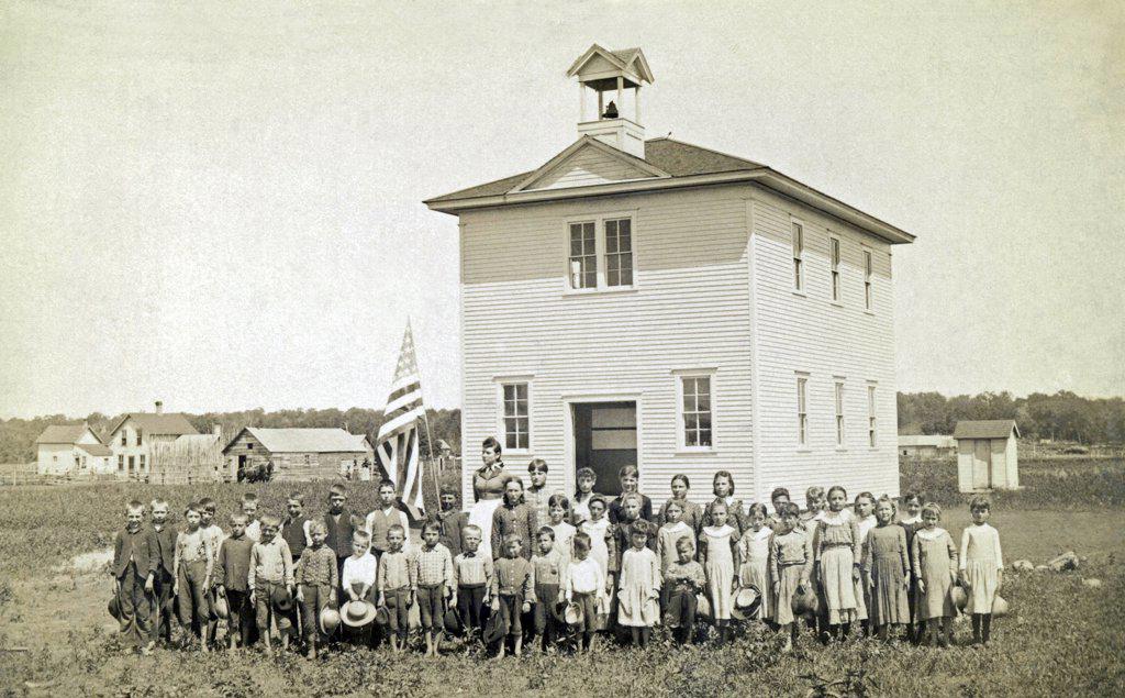 United States:  c. 1890. A one room schoolhouse in the prairie with the class and teacher out front for their portrait.