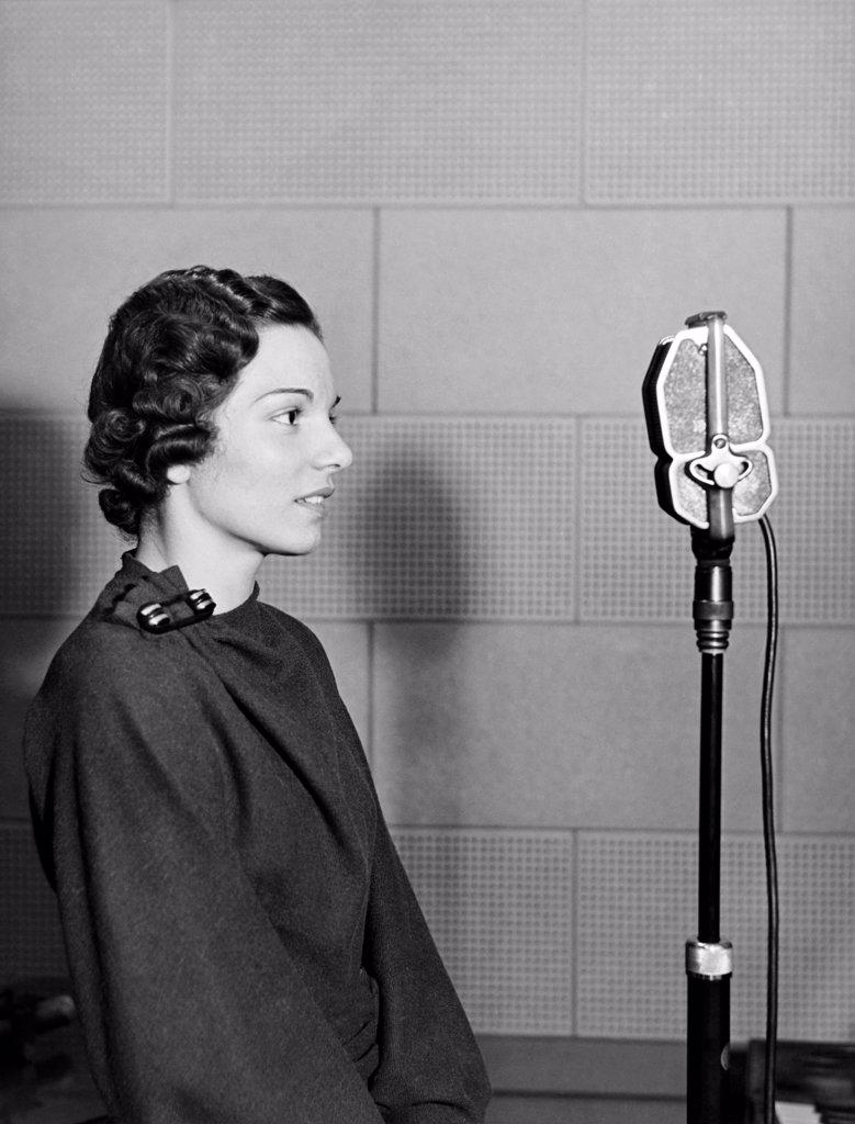 New York, New York:  c. 1937 A woman stands in the WOV studio in front of the microphone.