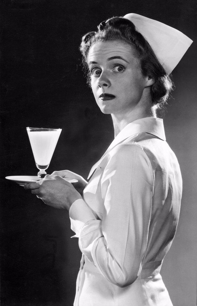 United States:  c.  1947 A nurse looking surprised as she is photographed carrying a glass of milk on a tray.