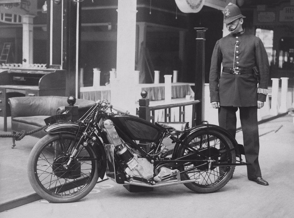 London, England:  c. 1937 A London policeman looks at a new sport model motorcycle that will do 80 mile per hour. It is on display at the Motor Cycle Show at Olympia Centre.