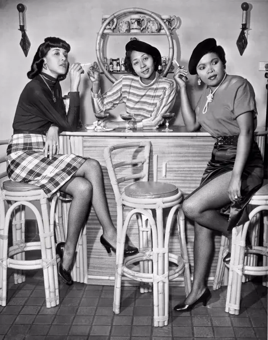 Los Angeles, California:  c. 1960. Three stylish African American women sitting with their drinks and cigarettes