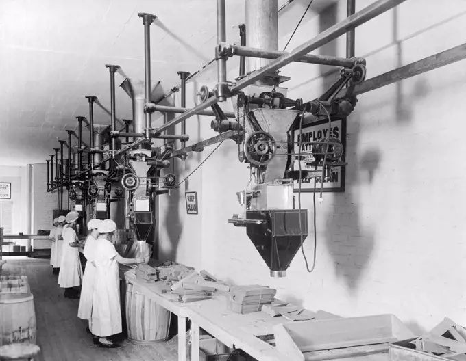 United States:  c. 1913 Women employees using Scott filling machines in a factory.