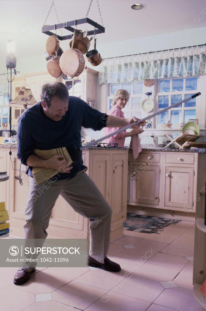 Stock Photo: 1042-11096 Mid adult man pretending to play the guitar with a broom and a mid adult woman standing behind him