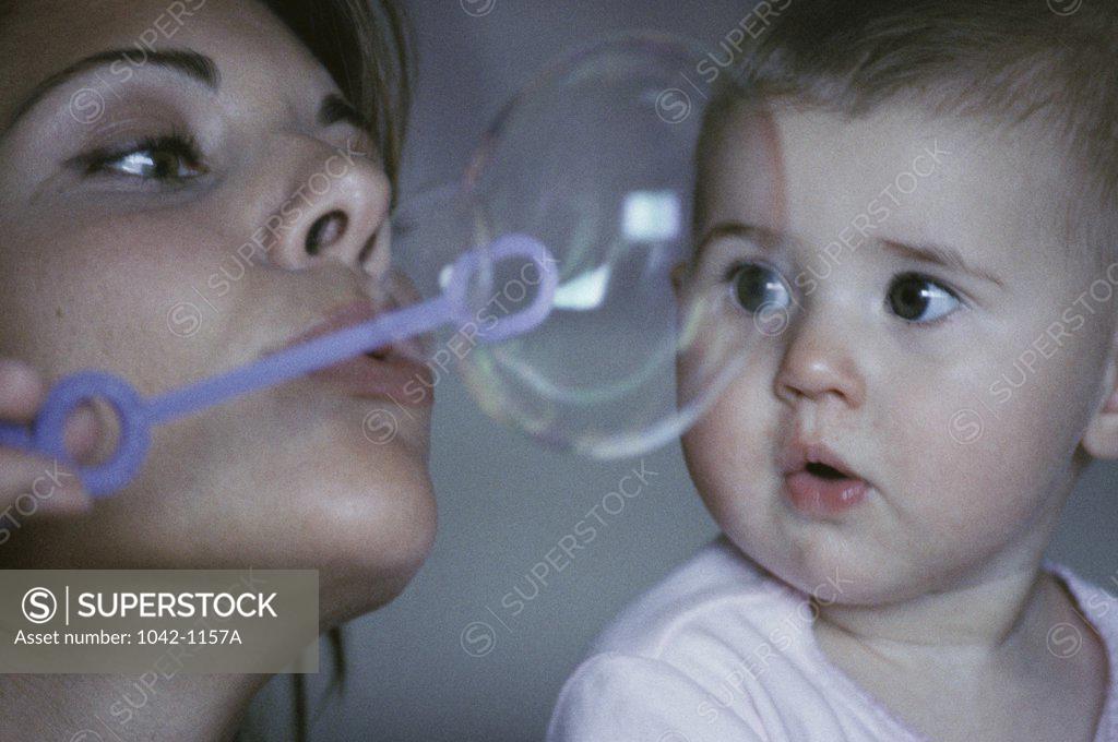 Stock Photo: 1042-1157A Close-up of a mid adult woman blowing bubbles with a bubble wand and her daughter looking at her