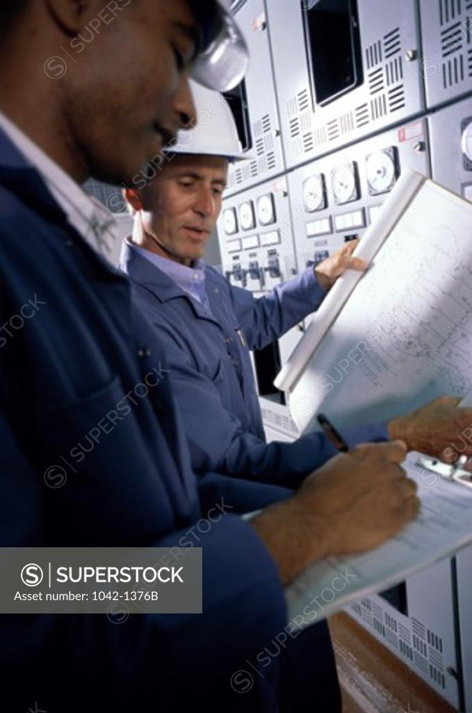 Stock Photo: 1042-1376B Side profile of two mid adult men standing in a factory holding blueprints