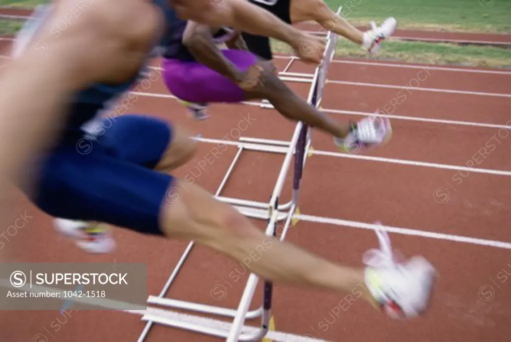 Side profile of three people jumping a hurdle