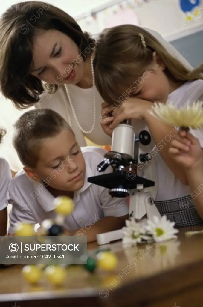 Children looking into a microscope with their teacher