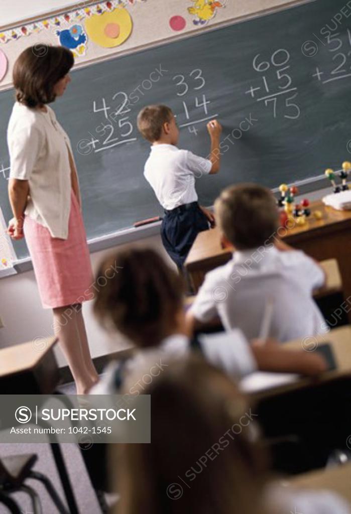 Stock Photo: 1042-1545 Boy writing on a blackboard in a classroom and a teacher standing beside him
