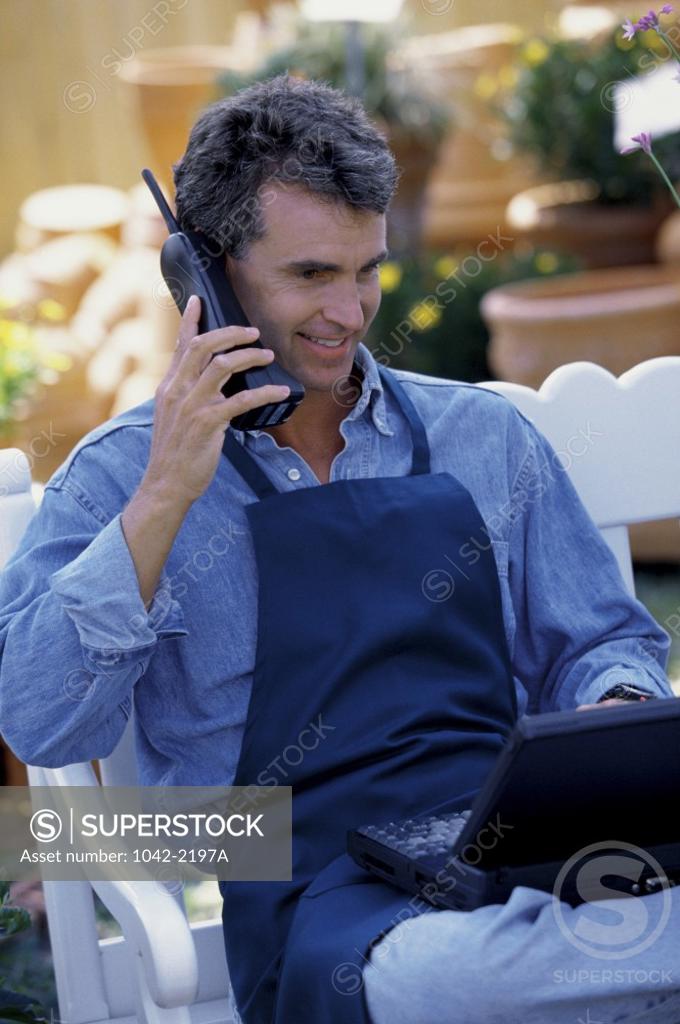 Stock Photo: 1042-2197A Mature man using a laptop while talking on a telephone