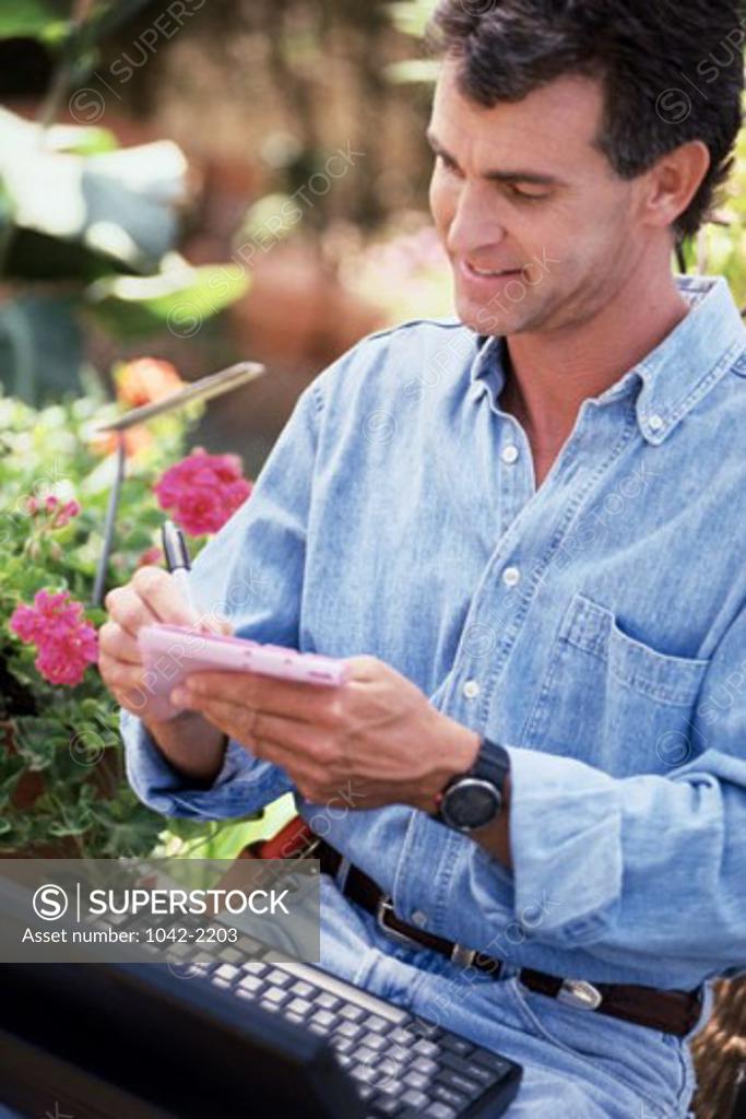 Stock Photo: 1042-2203 Close-up of a mid adult man writing on a notepad in a flower shop