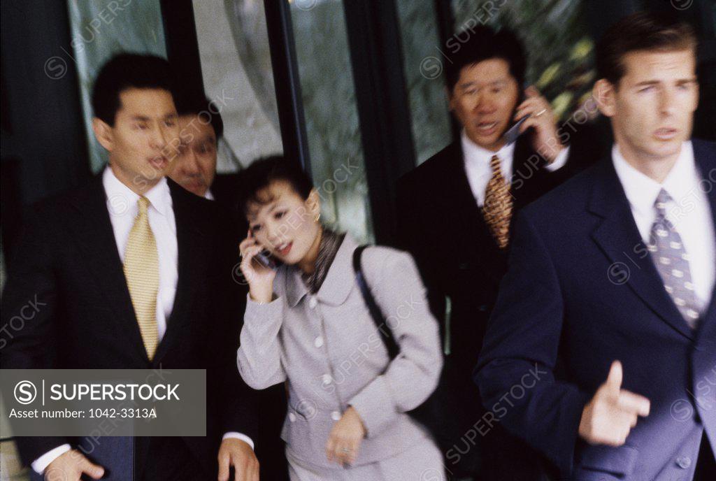 Stock Photo: 1042-3313A Businessman and a businesswoman talking on mobile phones and walking with their colleagues