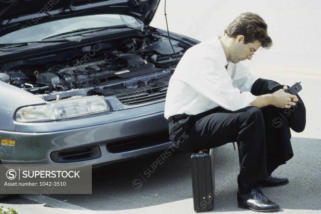 Stock Photo: 1042-3510 Side profile of a businessman sitting on briefcase in front of a car