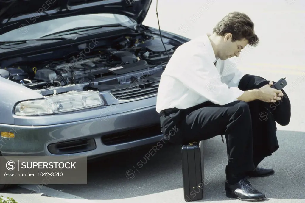 Side profile of a businessman sitting on briefcase in front of a car