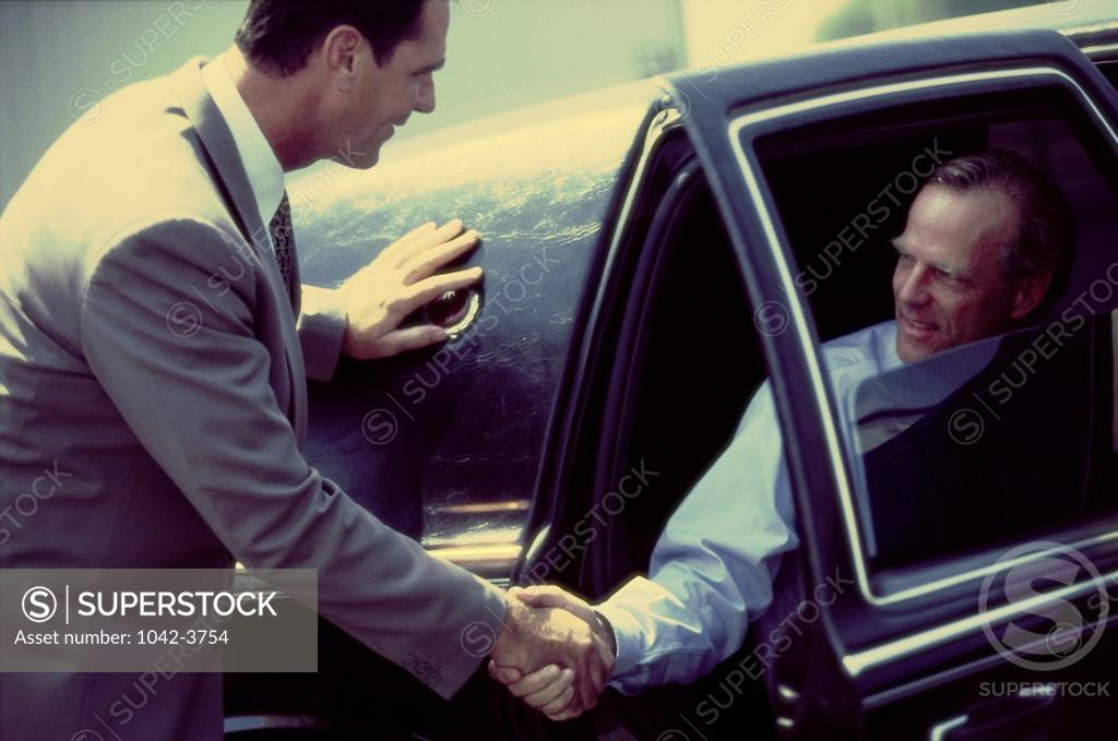 Stock Photo: 1042-3754 Two businessmen shaking hands sitting in a car