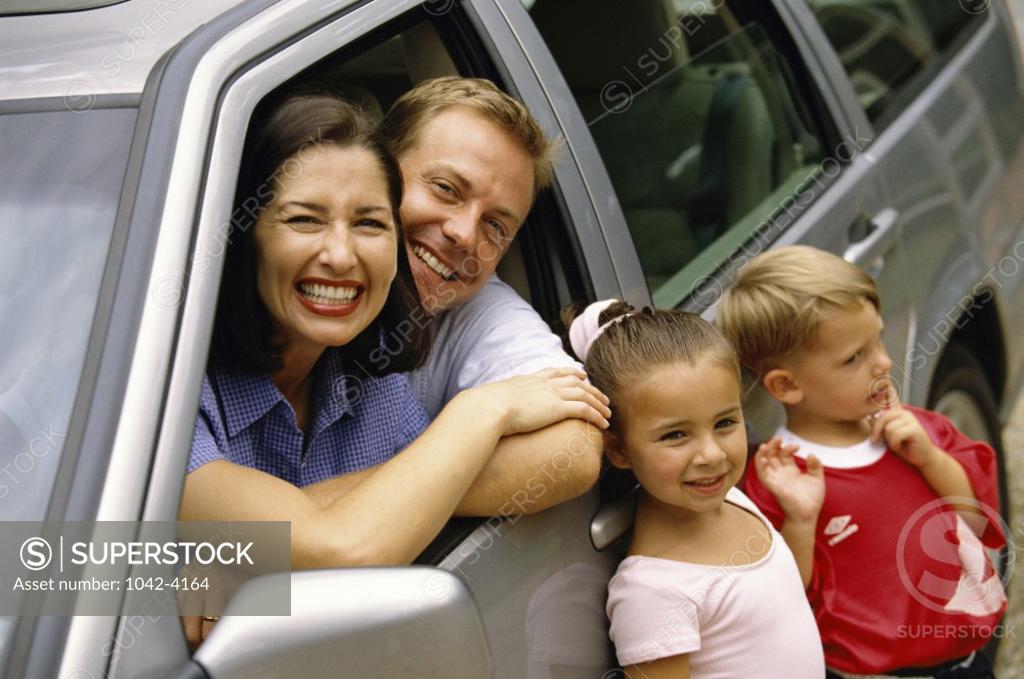 Stock Photo: 1042-4164 Portrait of parents sitting in a car with their son and daughter standing beside them