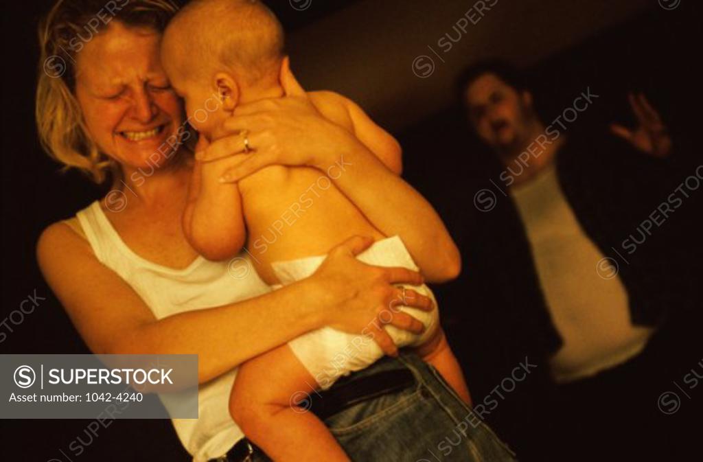 Stock Photo: 1042-4240 Mother carrying her baby boy with a mid adult man shouting behind her