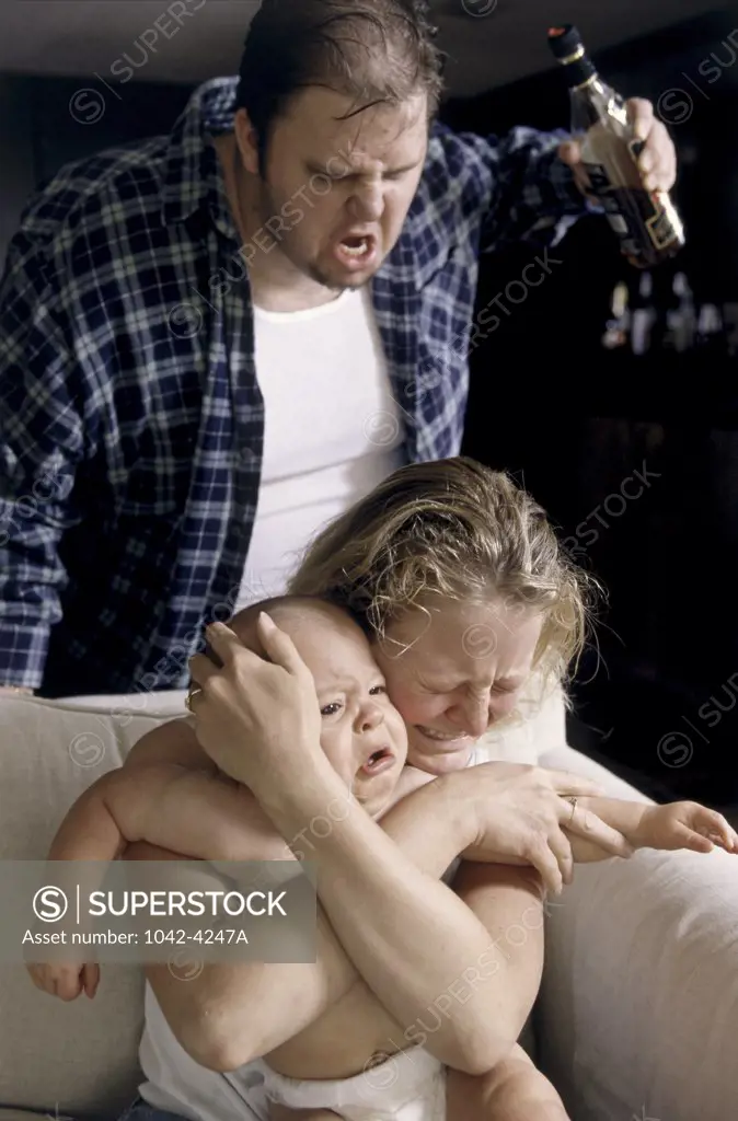 Mother holding her baby boy with a mid adult man shouting behind her