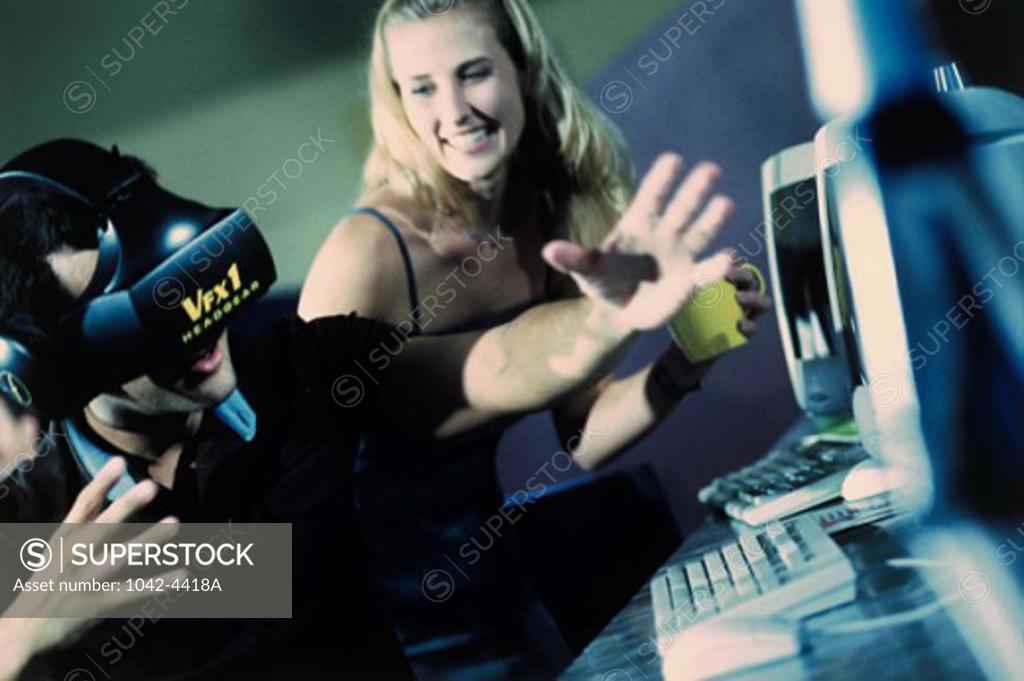 Stock Photo: 1042-4418A Side profile of a young man wearing a virtual reality simulator with a young woman sitting beside him in front of computers