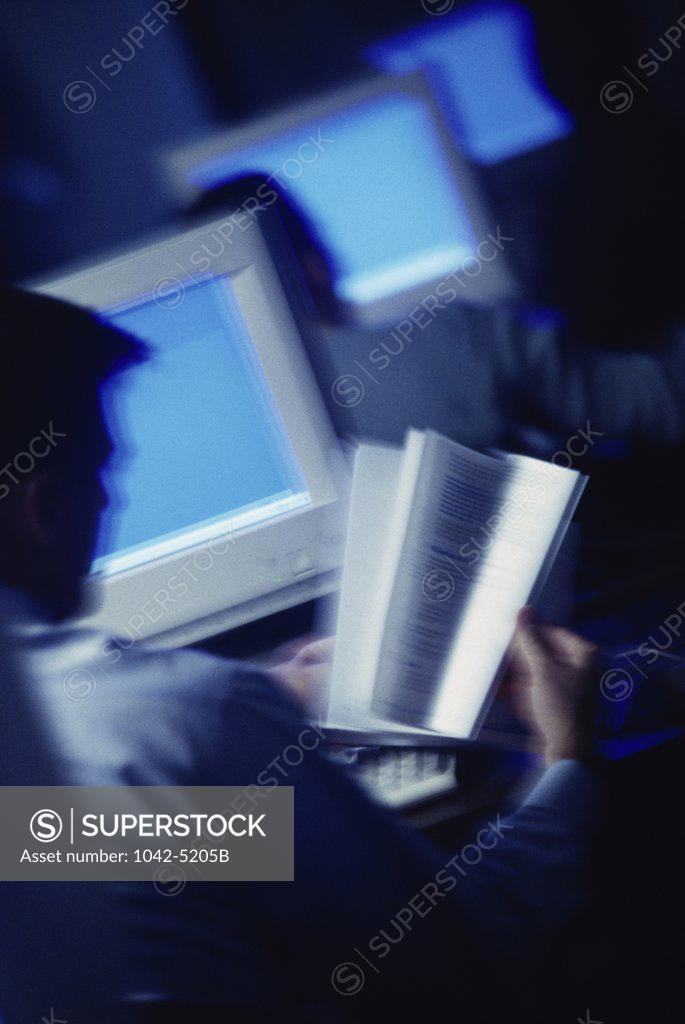 Stock Photo: 1042-5205B Rear view of a man reading a book in front of a computer monitor
