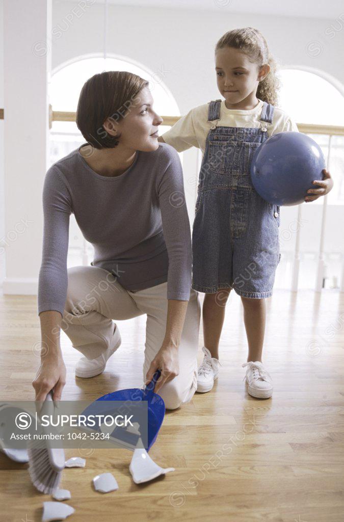 Stock Photo: 1042-5234 Mother sweeping up pieces of a broken vase with her daughter standing beside her