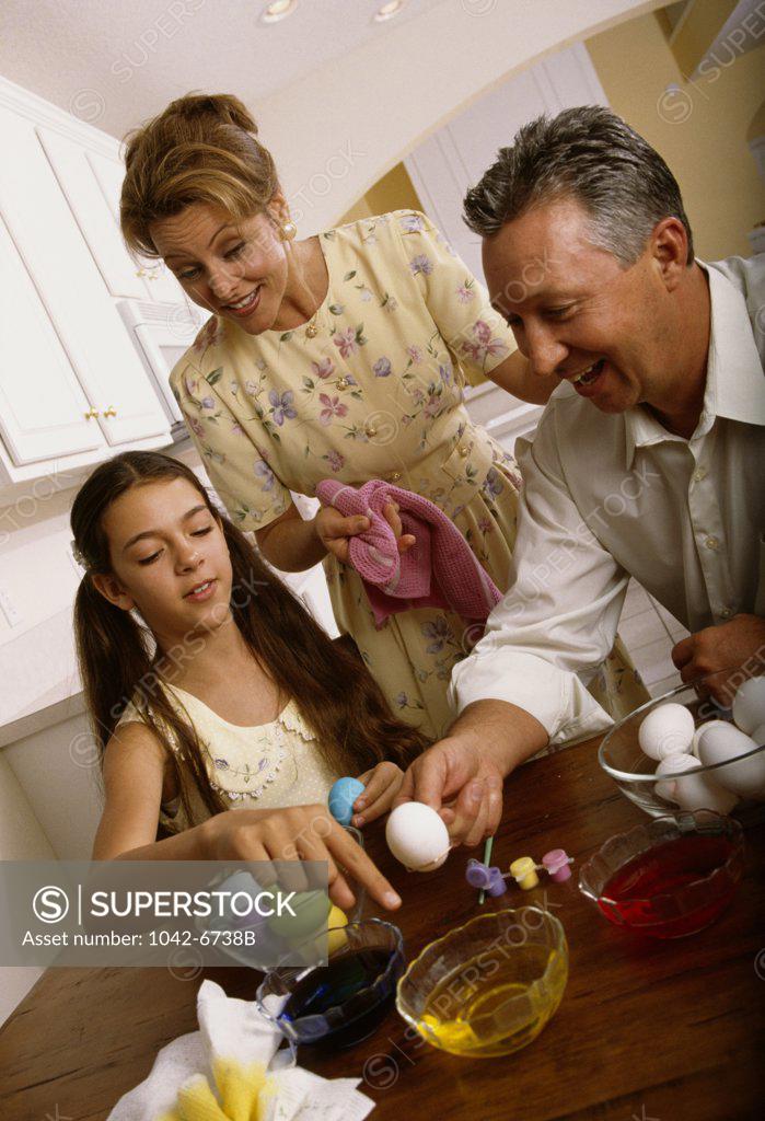 Stock Photo: 1042-6738B Girl with her father coloring Easter eggs with her mother standing beside her