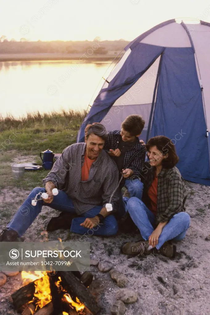 Mid adult couple roasting marshmallows in a campfire with their son