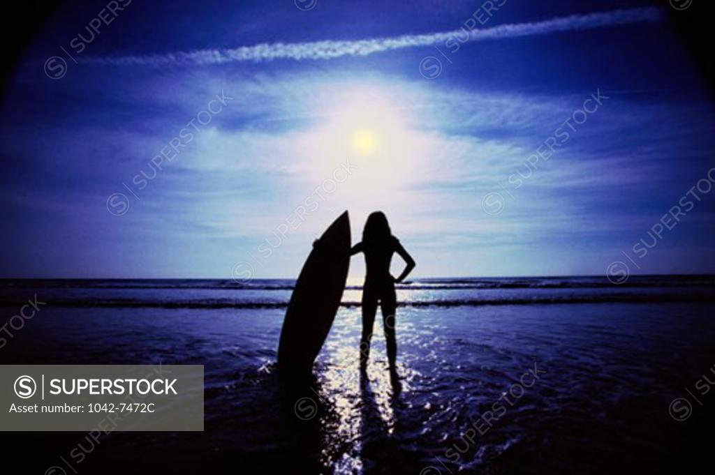 Stock Photo: 1042-7472C Silhouette of a woman holding a surfboard on the beach