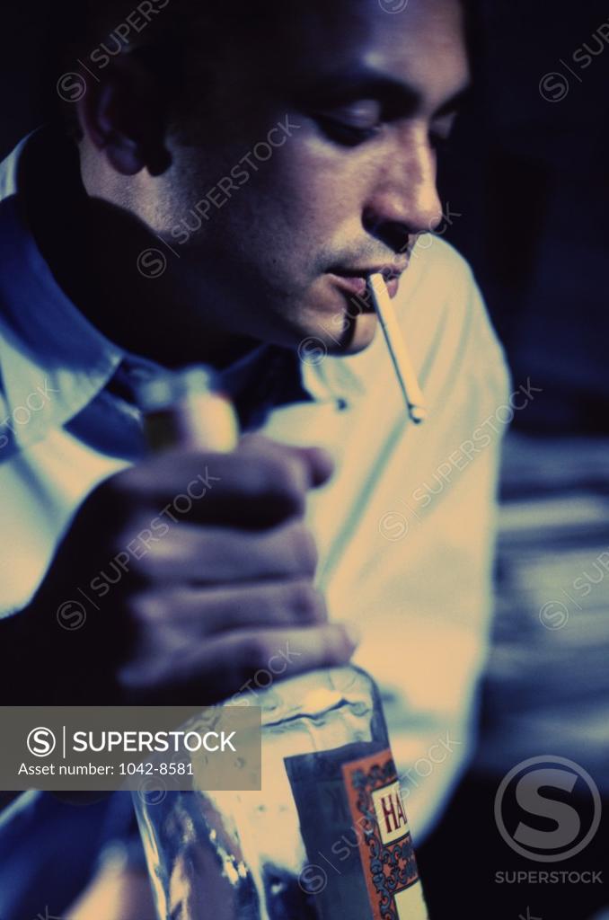 Stock Photo: 1042-8581 Young man with a cigarette in his mouth while holding a bottle of alcohol