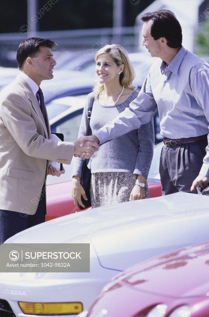 Stock Photo: 1042-9832A Two men shaking hands over the bonnet of a car with a woman standing besides them