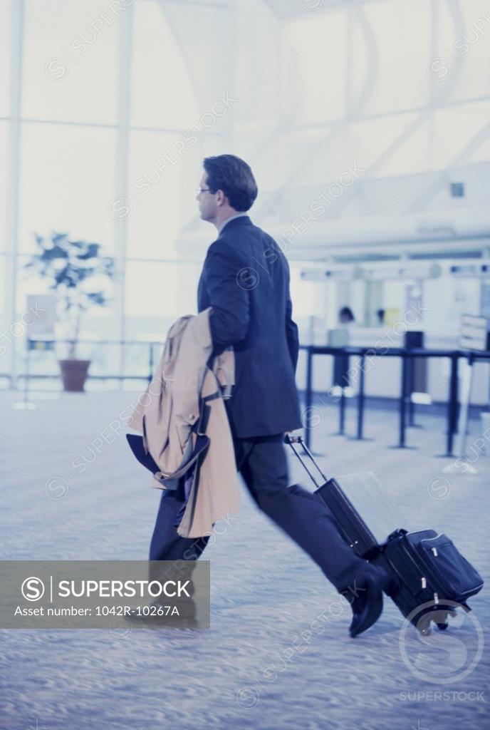 Stock Photo: 1042R-10267A Rear view of a businessman in an airport pulling a suitcase