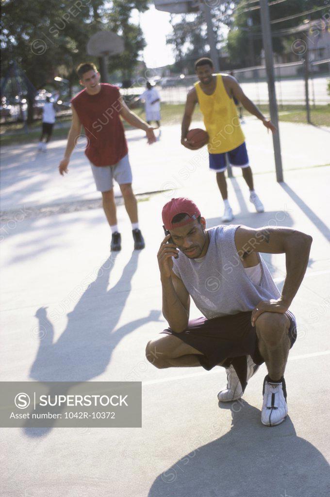 Stock Photo: 1042R-10372 Young man talking on a mobile phone with two young men standing behind him