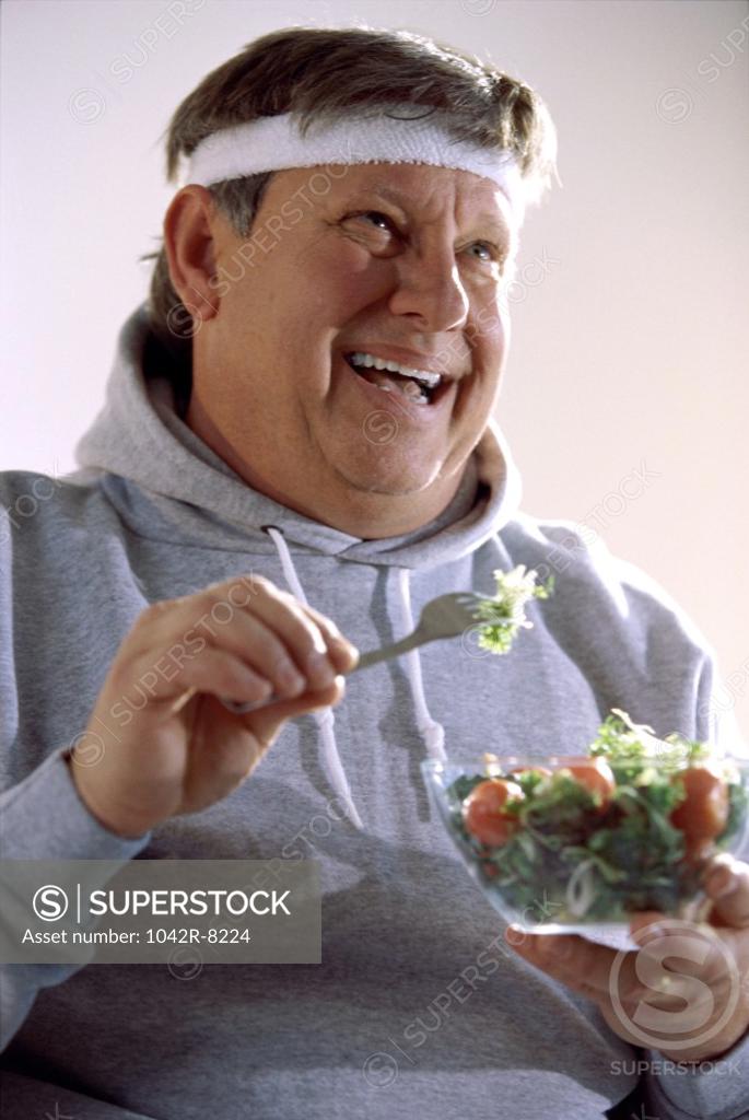 Stock Photo: 1042R-8224 Mid adult man eating salad from a bowl with a fork