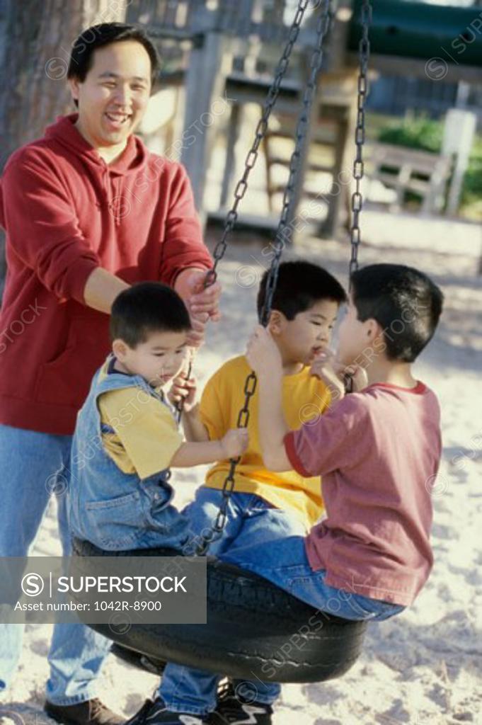 Stock Photo: 1042R-8900 Father playing with his three sons on a swing