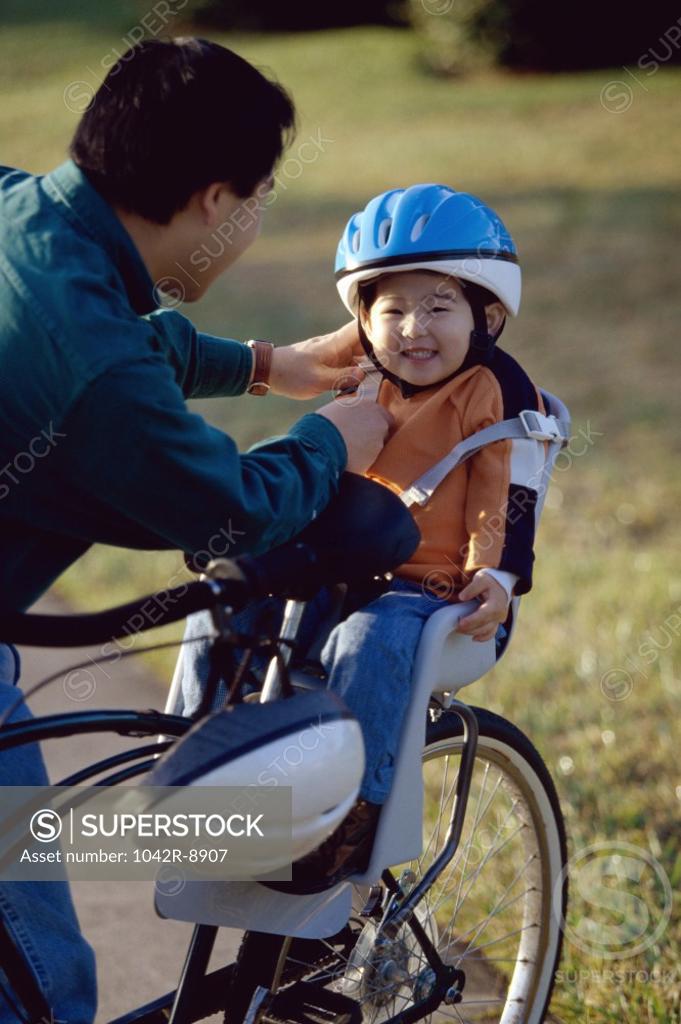 Stock Photo: 1042R-8907 Father fastening the strap of a cycling helmet on his daughter