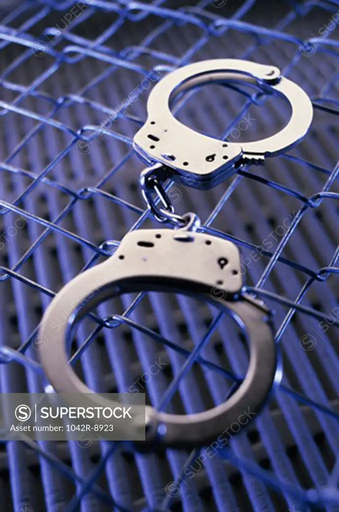 Close-up of a pair of handcuffs on a chain-link fence