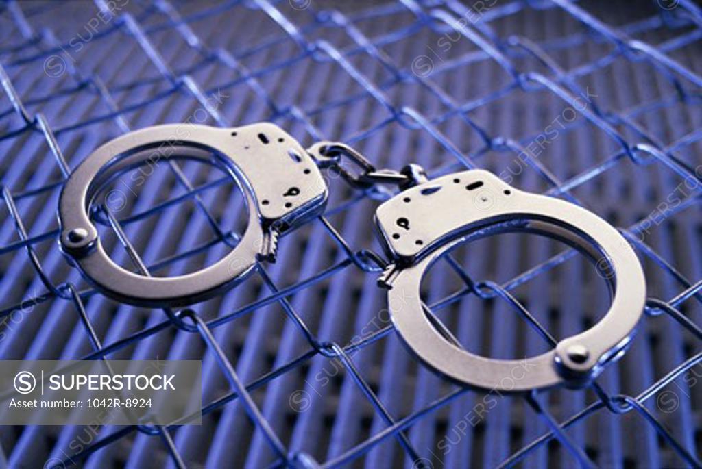 Stock Photo: 1042R-8924 Close-up of a pair of handcuffs on a chain-link fence