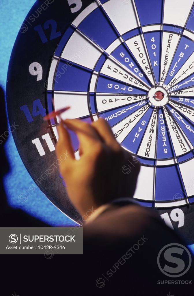 Stock Photo: 1042R-9346 Human hand holding a dart in front of a dartboard