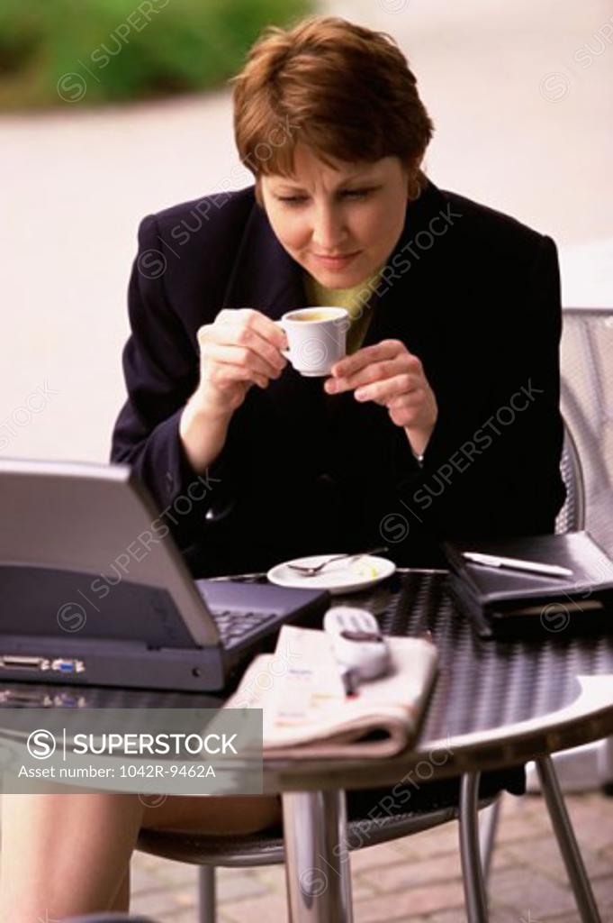 Stock Photo: 1042R-9462A Businesswoman holding a cup of coffee and looking at a laptop