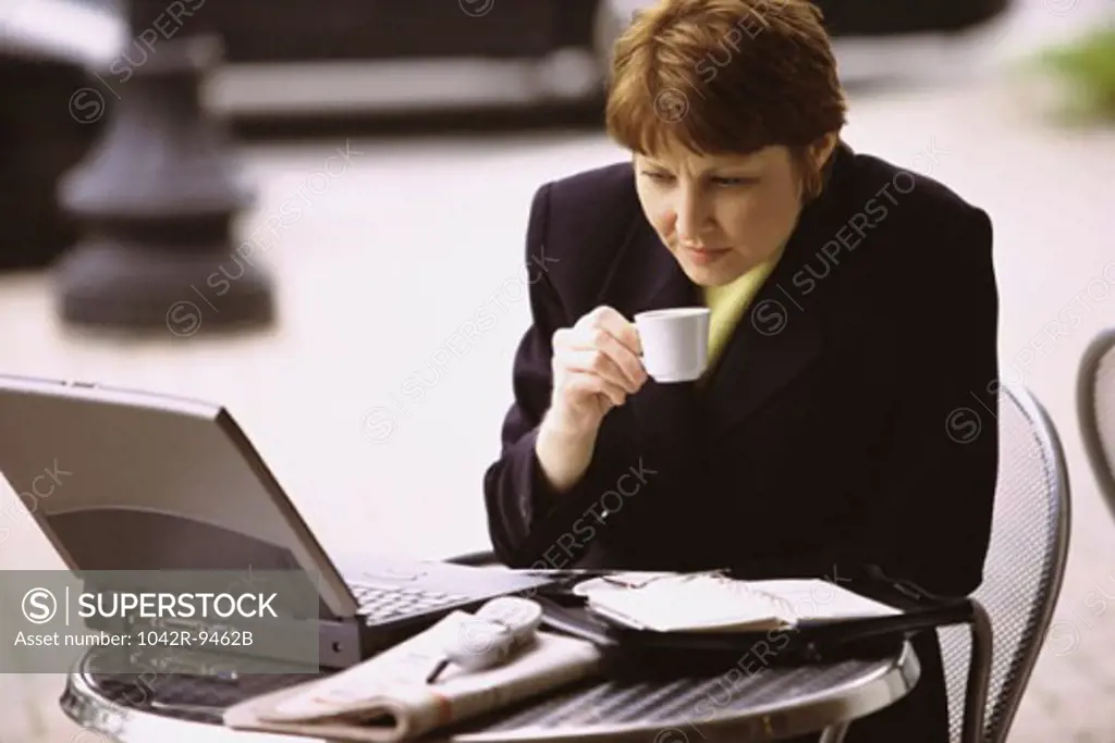 Businesswoman holding a cup of coffee looking at a laptop