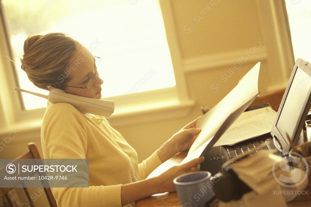 Stock Photo: 1042R-9746 Side profile of a businesswoman talking on a telephone and holding a document