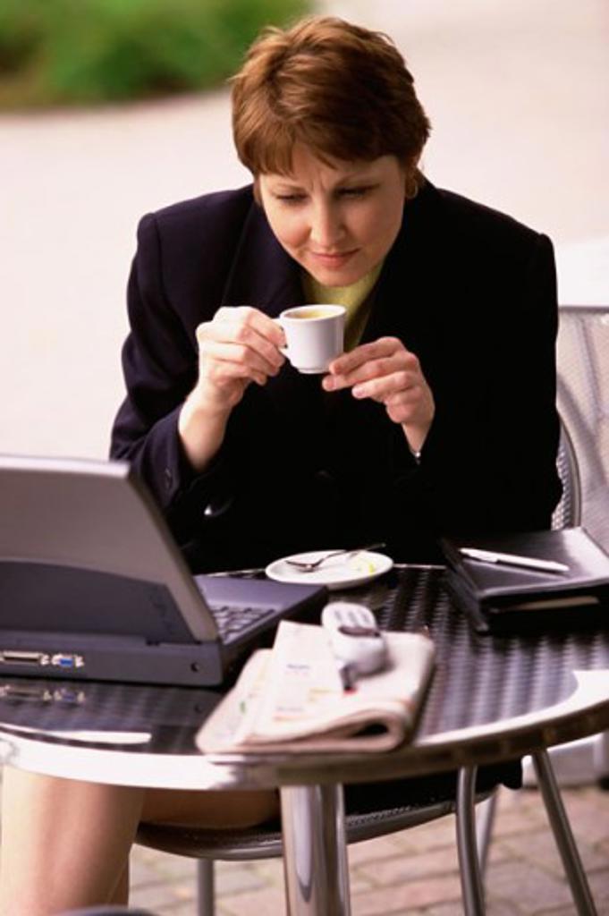 Businesswoman holding a cup of coffee and looking at a laptop