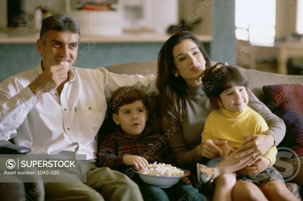 Stock Photo: 1043-105 Parents with their son and daughter sitting on a couch eating popcorn