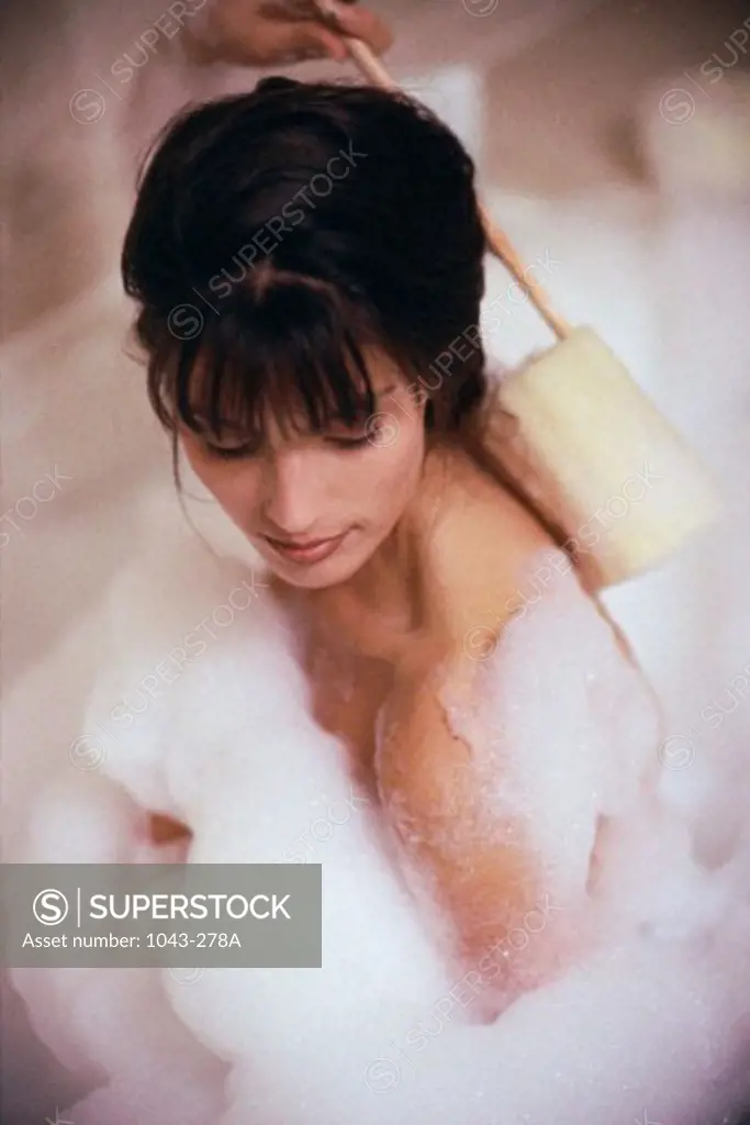 Close-up of a young woman scrubbing her back in a bubble bath