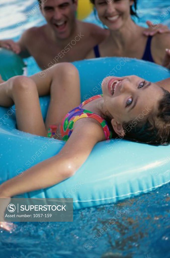 Stock Photo: 1057-159 Portrait of a girl sitting on an inflatable ring in a swimming pool with her parents behind her