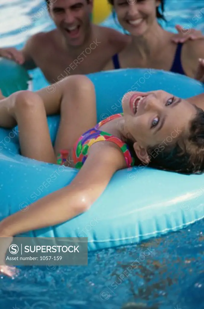 Portrait of a girl sitting on an inflatable ring in a swimming pool with her parents behind her