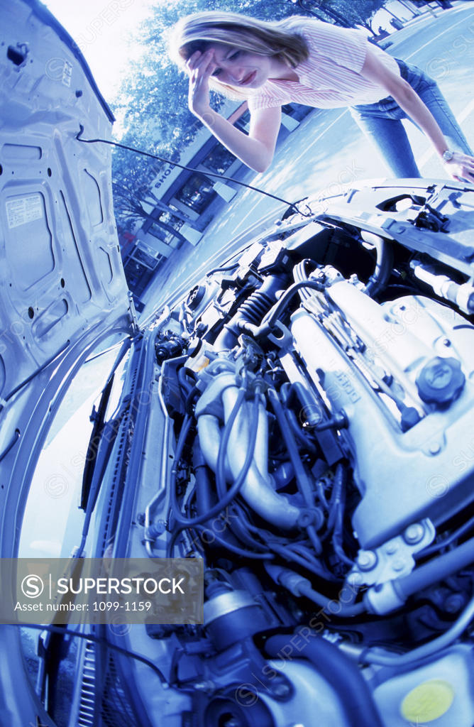 Stock Photo: 1099-1159 Young woman looking under the hood of her car
