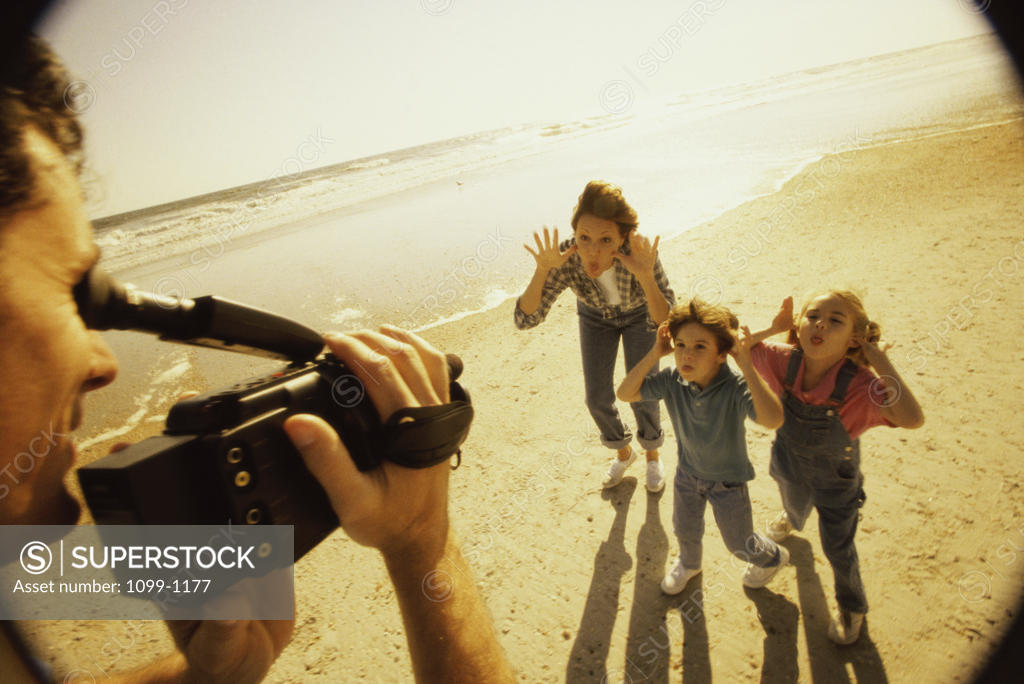 Stock Photo: 1099-1177 Father filming his wife and children on the beach