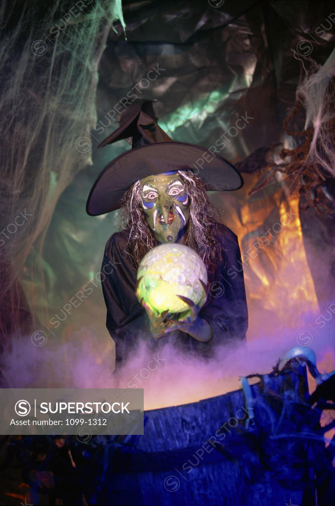 Stock Photo: 1099-1312 Witch holding a crystal ball standing in front of a cauldron